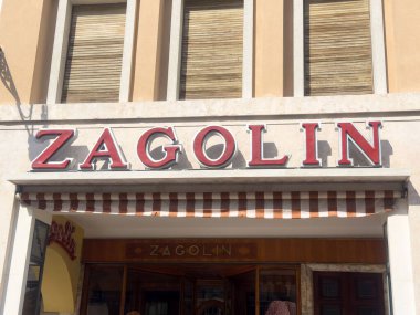 Çizgili tente ve gün ışığında kalın harflerle Zagolin mağazası önü.