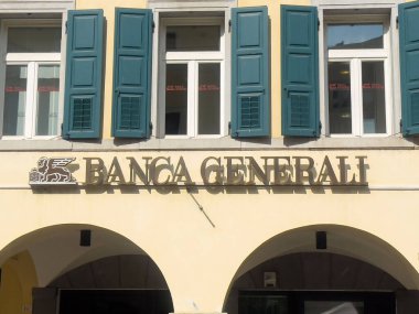 Banca generali mavi panjurlu ve kemerli pencereli bina cephesi.