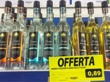 Mağaza rafında çeşitli grappa şişeleri ve İtalyan bakkalında özel teklif levhası var..