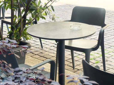 Yeşilliğin ortasında boş masaları ve sandalyeleri olan açık bir kafe..