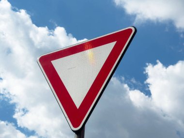Bulutlu mavi gökyüzüne karşı kırmızı ve beyaz verim işareti.