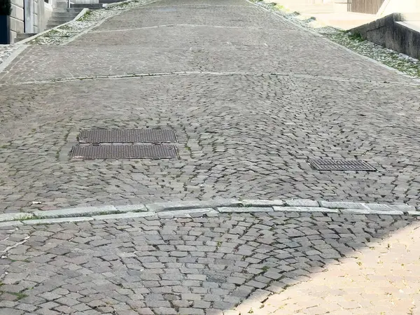 Eğimli bir tepede rögar kapağı olan kaldırımsız bir cadde..