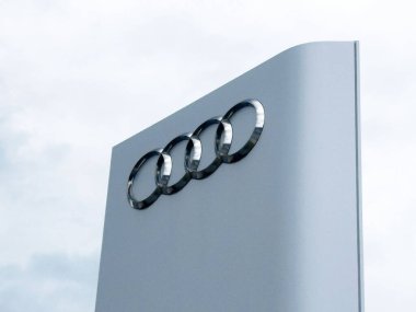 Bulutlu gökyüzüne karşı modern tabela üzerine Audi logosu.