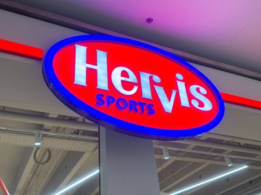 Parlak kırmızı ve mavi logolu Hervis spor mağazası tabelası.