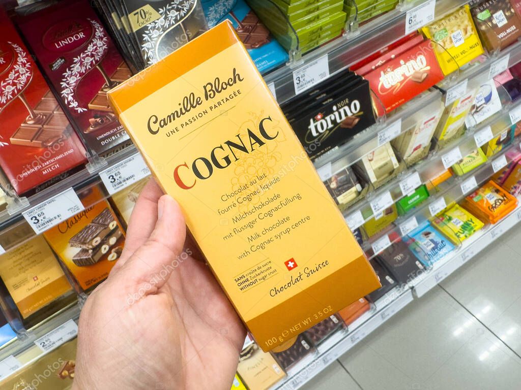 Adult caucasian hand holding swiss cognac chocolate box in supermarket aisle.