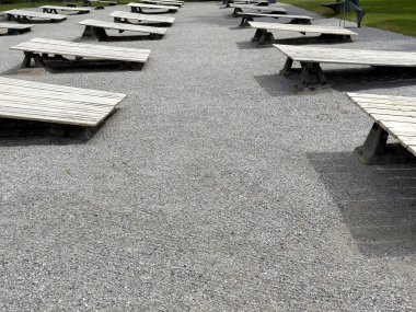 Parktaki çakıl yolunda boş ahşap masalarla dışarıda piknik yapmak..