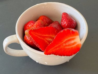 Gri yüzeyde beyaz seramik bardakta taze çilekler..