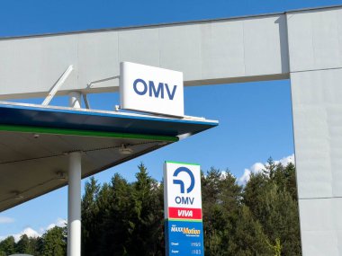 Mavi gökyüzü ve orman arka planına karşı Omv benzin istasyonu işareti.