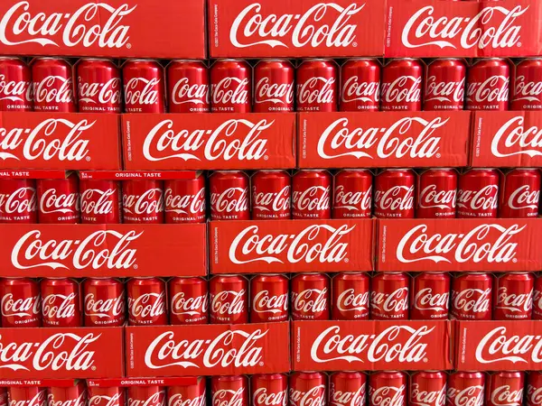 Satırlarda istiflenmiş Coca-Cola kutuları simgesel kırmızı ambalajları gösterir.