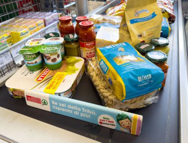 Süpermarket konveyöründe çeşitli sebze ürünleri: makarna, sos, aperatif ve yoğurt.