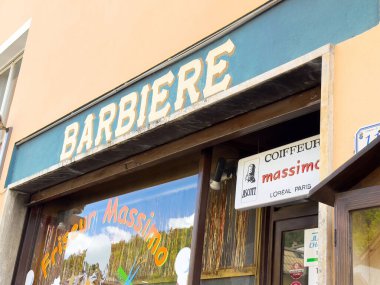 İki dilli işaret dili ve renkli pencere dekorasyonuyla geleneksel berber dükkânı dış görünüşü.