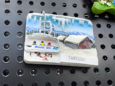 Teleferikli karlı dağ manzarası ve Tarvisio hatıra mıknatısı kabini..
