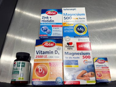Metalik bir yüzeyde çeşitli Alman vitamin ve takviye paketleri sergilenmektedir..