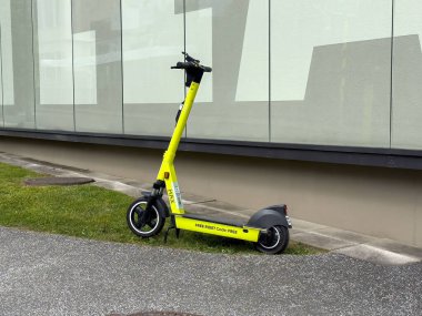Sarı elektrikli scooter, pencereli binanın yanındaki kaldırıma park edilmiş..