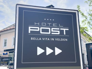 Arka planda ağaç ve bina olan otel tabelası, Velden.