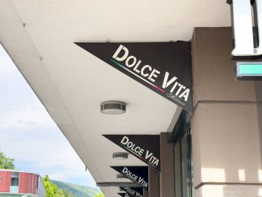 Dolce vita mağaza önü tabelası üzerinde mavi gökyüzü ve arka planda ağaçlar.