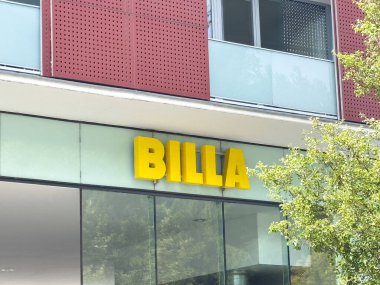 Modern binanın dış cephesinde cam paneller ve ağaç ile Billa mağaza önü tabelası.