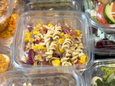 Mısır, kırmızı soğan ve plastik kabın içinde domatesli taze makarna salatası..