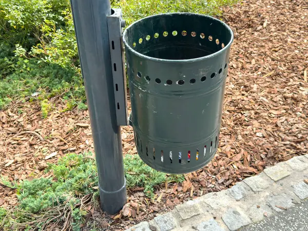 Park ayarlarına iliştirilmiş yeşil metal çöp kutusu.