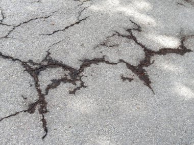 Görünür hasar ve doku detaylarıyla çatlak asfalt yüzeyi.
