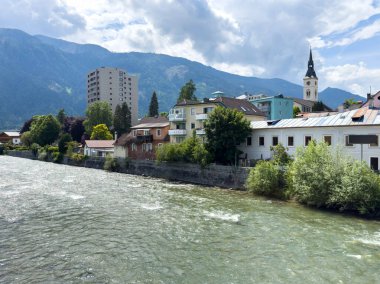 Arka planda dağlar ve kilise olan manzaralı nehir kenarı..