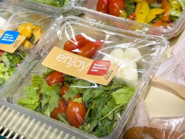 Plastik kabın içinde taze domates ve mozzarella salatası ve karışık sebzeler..