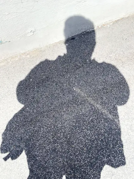 Parlak güneş ışığı altında asfaltta duran erkek figürü..