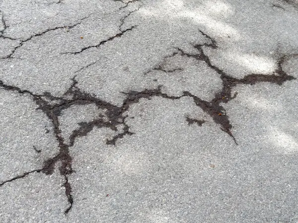 Görünür hasar ve doku detaylarıyla çatlak asfalt yüzeyi.