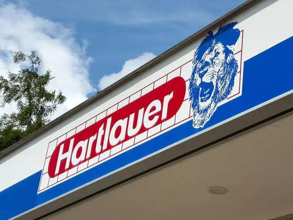 Mavi gökyüzünde aslan amblemi olan Hartlauer mağazası tabelası.