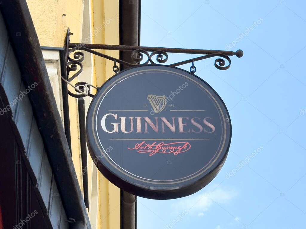Pub sign for guinness beer on building exterior against blue sky.