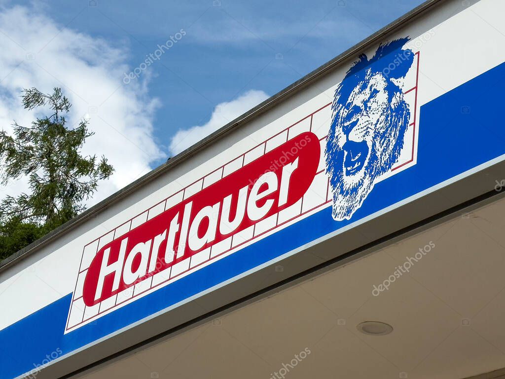 Hartlauer store sign with lion logo against blue sky.