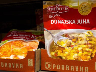 Bakkal koridorunda Podravka çorba ambalajı görüntüsü, odak noktasında çeşitli malzemeler var..