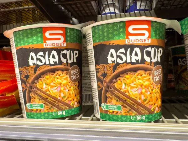 Hazır erişte bardakları yemek çubukları ve sebzelerle dolu raflarda..