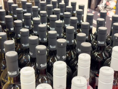 Rafta siyah beyaz kapaklı çeşitli şarap şişeleri var..