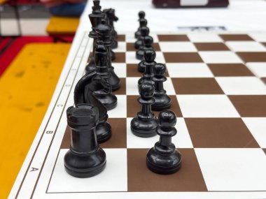 Kahverengi ve beyaz tahtadaki siyah satranç taşları stratejik oyuna hazır..