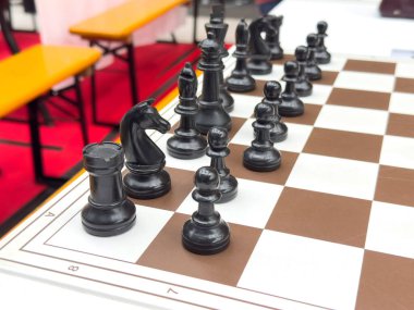 Siyah satranç taşları, kapalı bir etkinlikte kahverengi ve beyaz bir levhaya yerleştirilmiş..