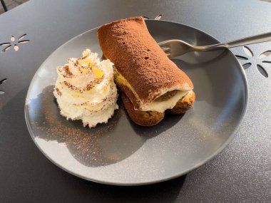 Tiramisu tatlısı, güneş ışığında siyah tabakta krem şanti..