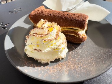 Güneş ışığında siyah tabakta krem şantili nefis tiramisu..