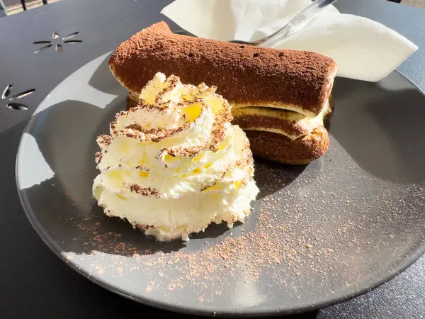 Güneş ışığında siyah tabakta krem şantili nefis tiramisu..