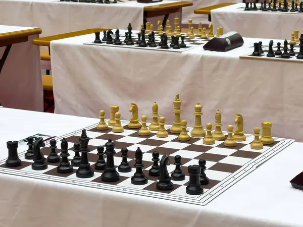 Beyaz masa örtülerinde birden fazla tahta bulunan satranç turnuvası kurulumu.