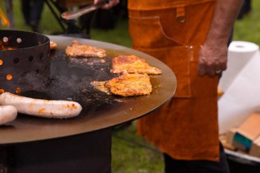 Açık havada barbekü yapan erkek eti turuncu önlüklü..
