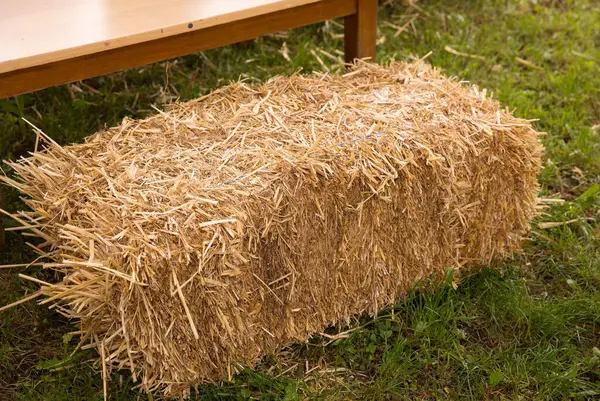 Çimlerin üzerinde dikdörtgen saman balyası. Açık havada ahşap bankın yanında..