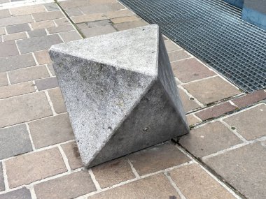 Beton piramit benzeri heykel rendelenmiş kaldırımın yanındaki tuğladan kaldırımda.