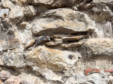 Doğal dokuyu ve çeşitli kaya renklerini gösteren eskimiş taş bir duvar..