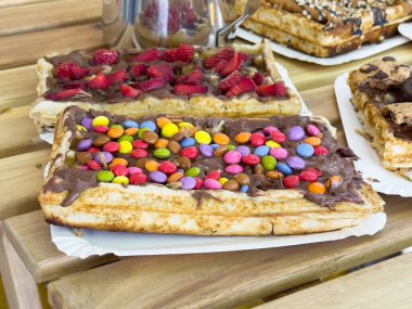 Lezzetli çikolata kaplı waffle, ahşap masada renkli malzemeler..