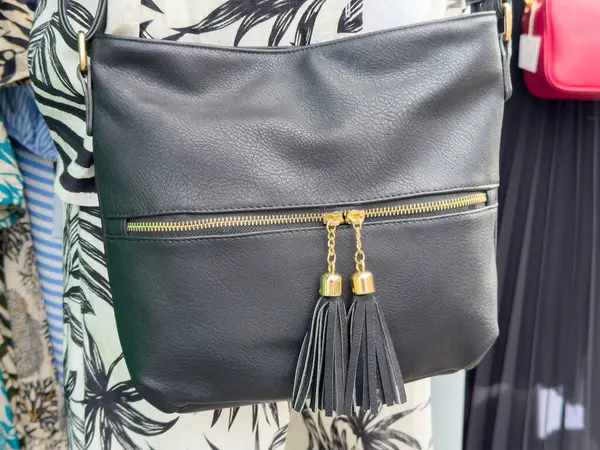 Şık siyah deri çanta, püskülleri ve desenli kumaş üzerinde altın aksanları var..