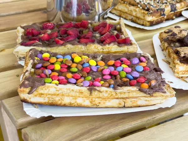 Lezzetli çikolata kaplı waffle, ahşap masada renkli malzemeler..