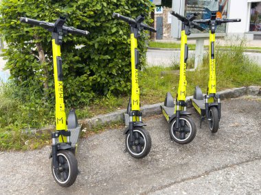 Yeşilliğin yanındaki kaldırıma park edilmiş dört sarı elektrikli scooter..