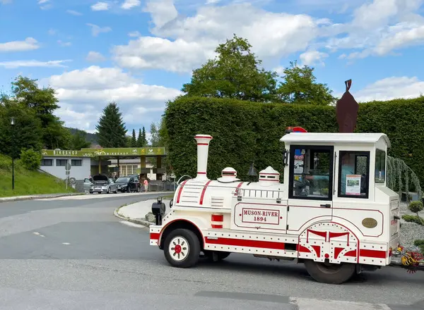 Beyaz turist treni park girişinde manzaralı yeşil ve kabarık bulutlu.