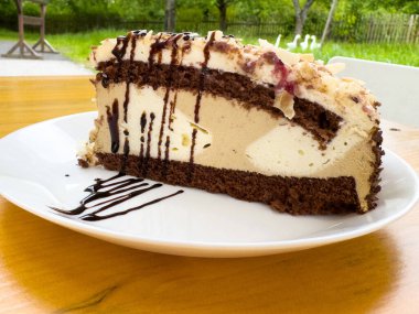 Dışarıdaki ahşap masada nefis bir dilim çikolata ve kremalı pasta..